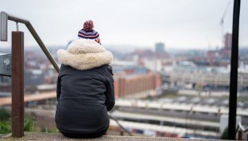 Young person with a winter coat on sat on stairs looking over a city