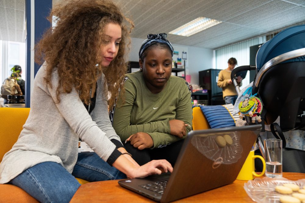 Two women working on a laptop in a busy room