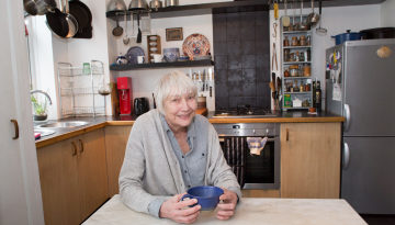 Older woman sat in her kitchen holding a mug