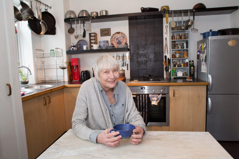 Older woman sat in her kitchen holding a mug