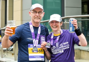 Man and woman runners wearing medals, holding beers
