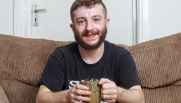 Young man sitting on a brown sofa holding a mug.