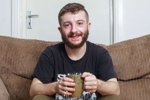 Young man sitting on a brown sofa holding a mug.