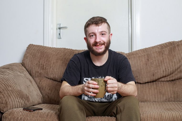 Young man sitting on a brown sofa holding a mug.