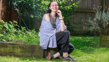 Rachel sitting on a wall in a garden smiling