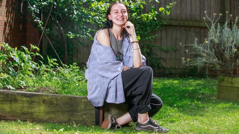 Rachel sitting on a wall in a garden smiling