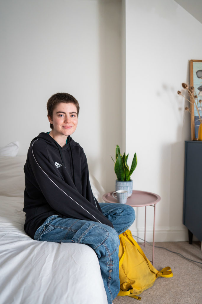 Jo sitting on a bed smiling towards the camera