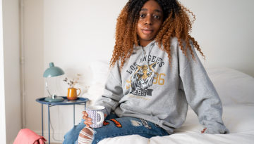 Young black woman sat on a bed looking at the camera