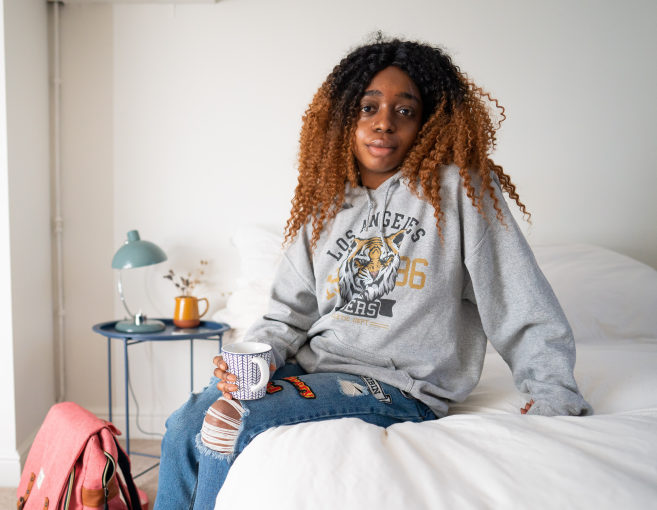Young black woman sat on a bed looking at the camera
