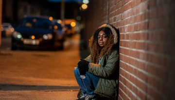 Young black women hunched by a wall on the street