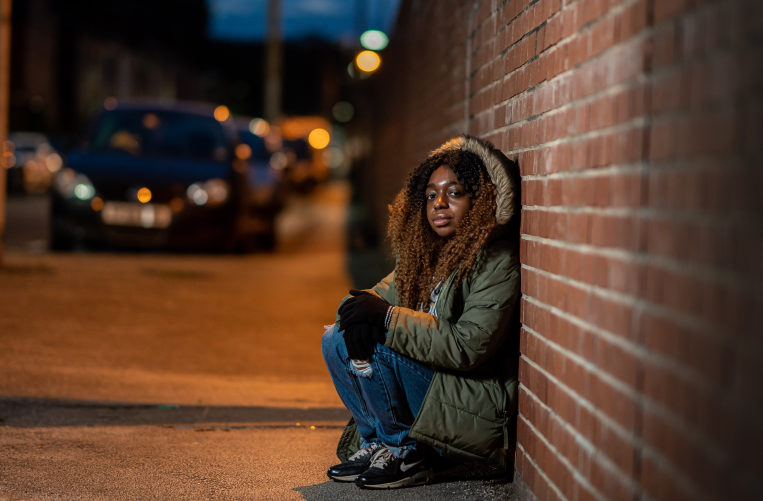 Young black women hunched by a wall on the street