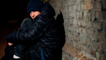 Young man sitting on the street hugging his knees