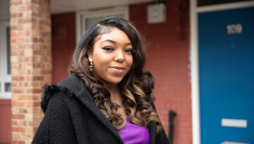 Claudia smiling to the camera standing outside a block of flats