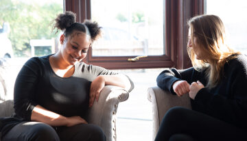 Two young women sitting on sofa talking and laughing