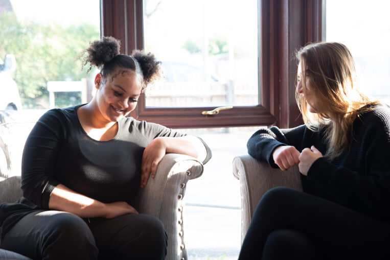 Two young women sitting on sofa talking and laughing