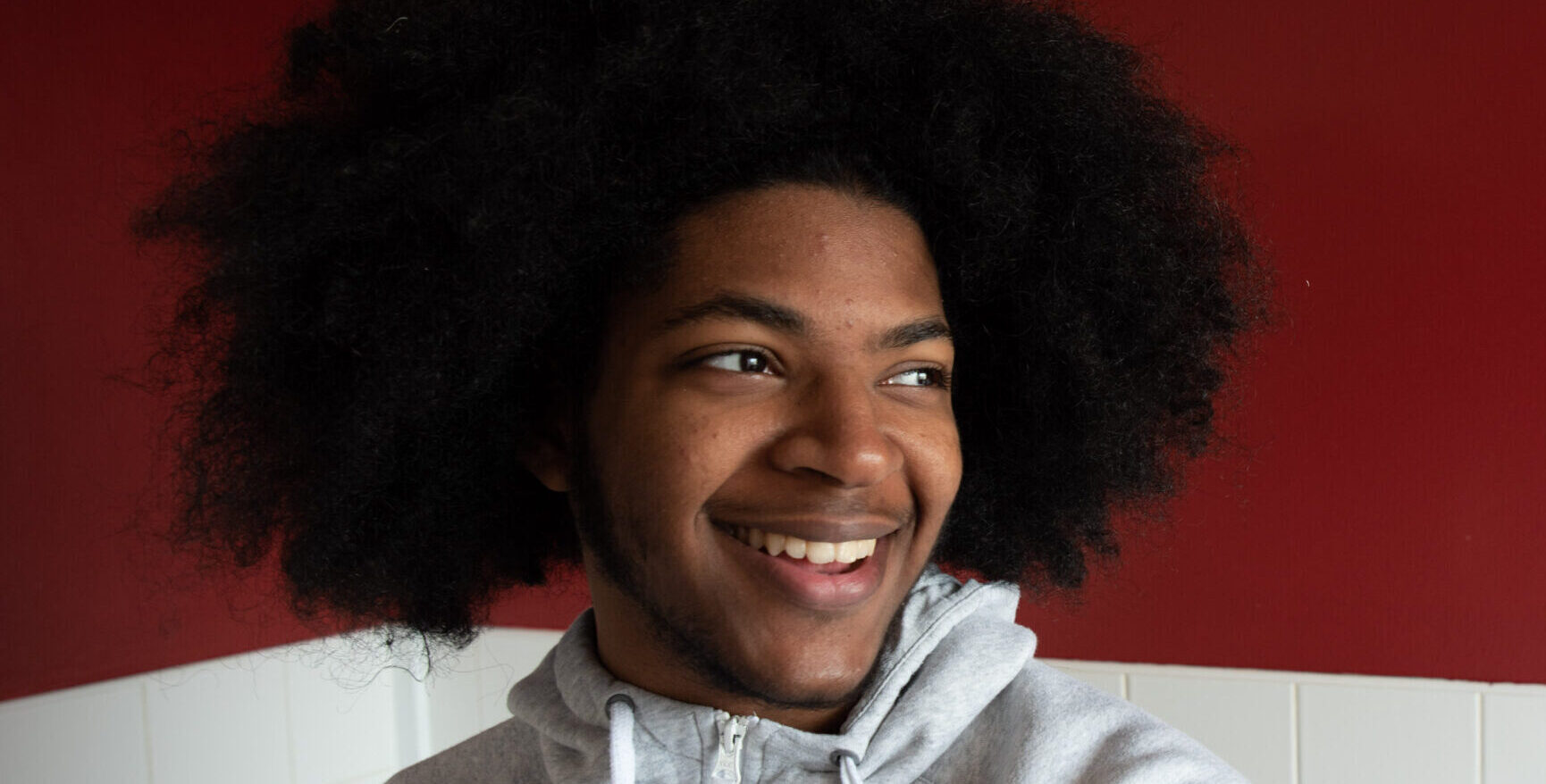 Young person with afro smiling stood in front a red