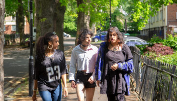 three young people walking along a sunny street