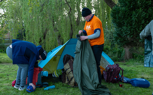 Man packing away a tent and sleeping bag