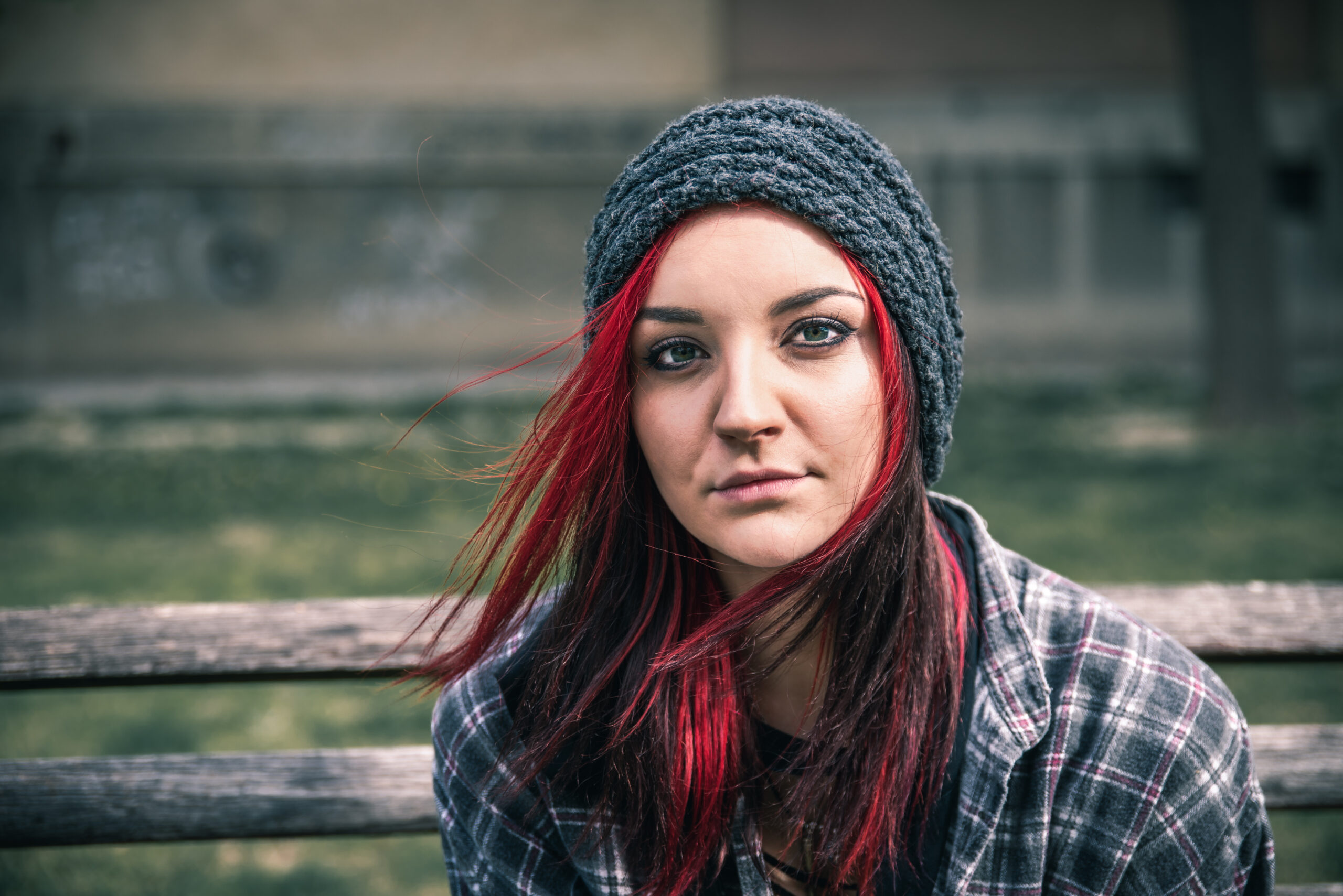 Young red hair girl sitting alone outdoors on the wooden bench with hat and shirt feeling anxious and depressed after she became a homeless person close up portrait