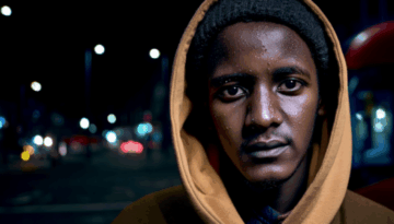 Alan looking pensive to camera with hood up a dark street