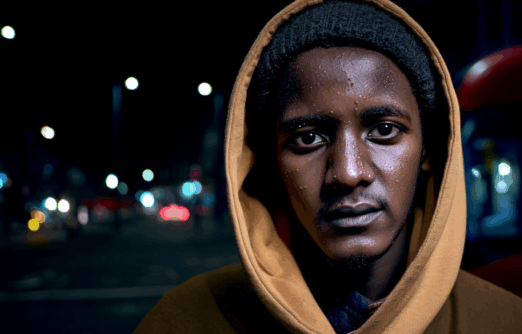 Alan looking pensive to camera with hood up a dark street