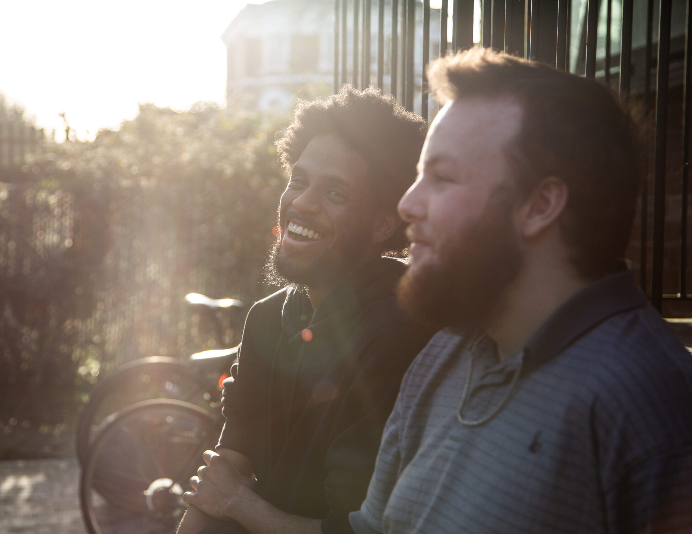 Two young men sat in the sunshine by bikes laughing together
