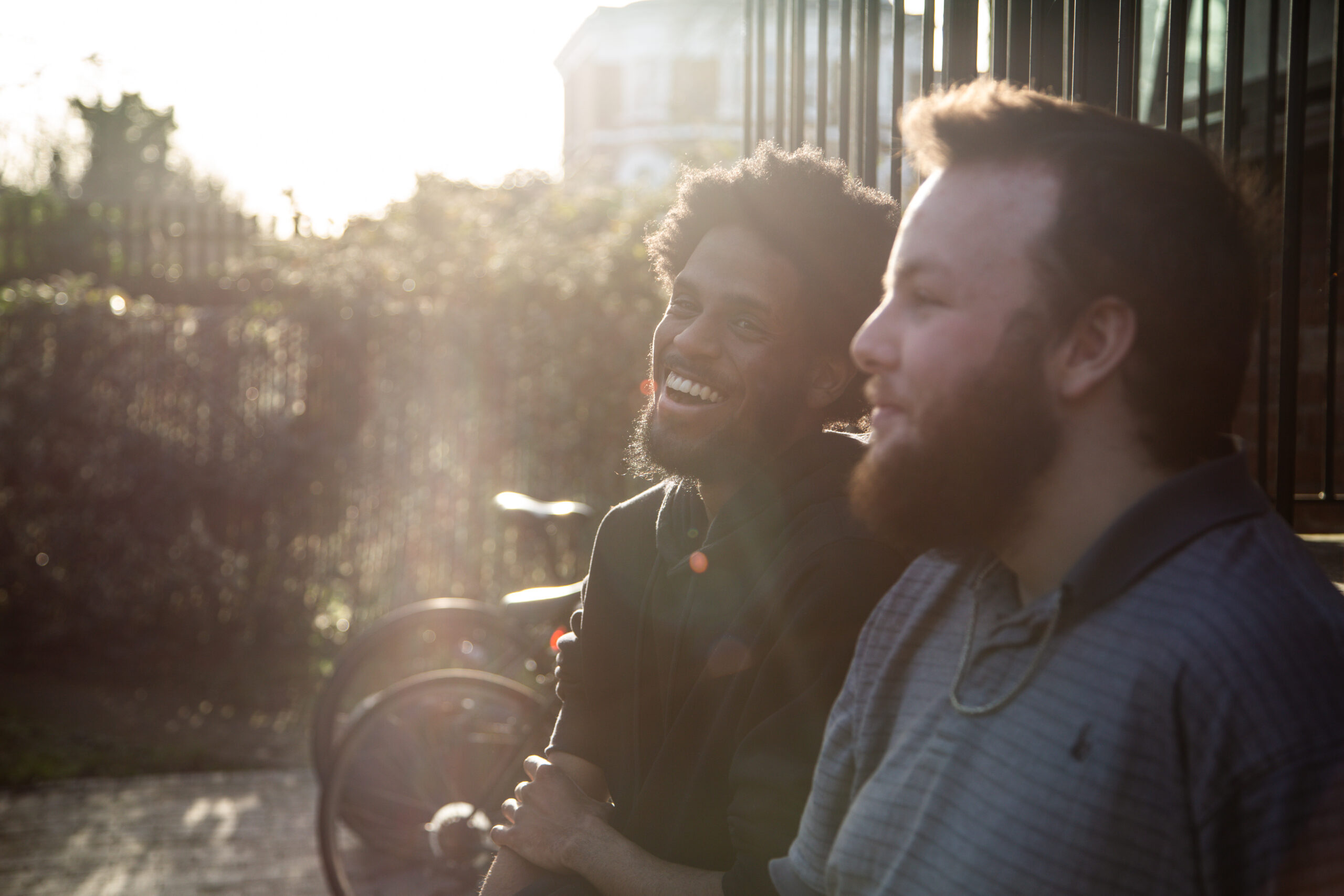 Two young men sat in the sunshine by bikes laughing together