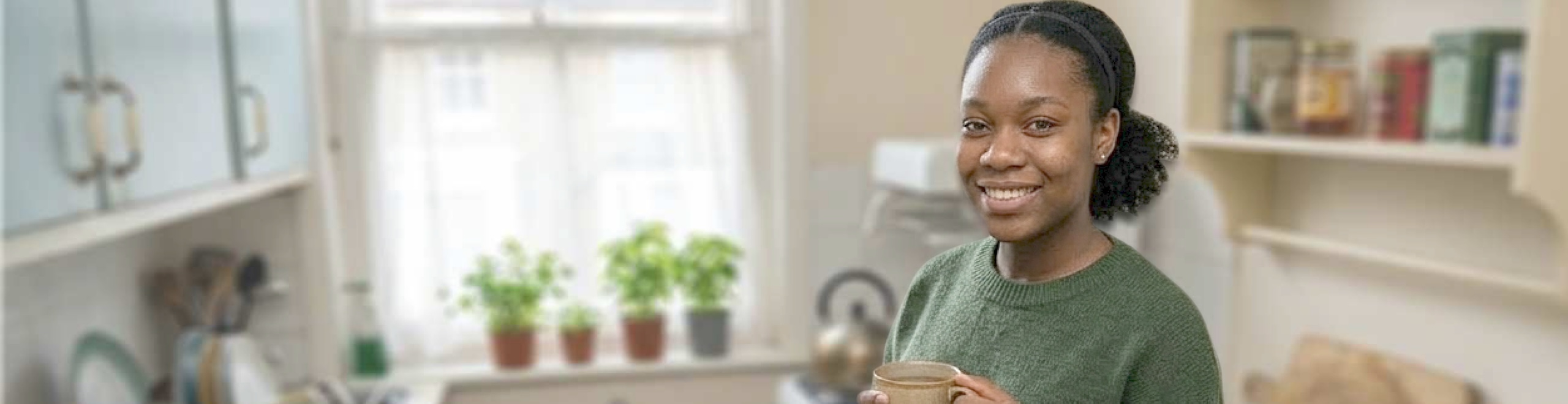 A young person who has recently moved into their home stood in their kitchen smiling and enjoying a cup of tea