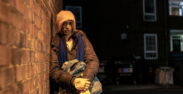 Young woman against a wall in the dark with her rucksack